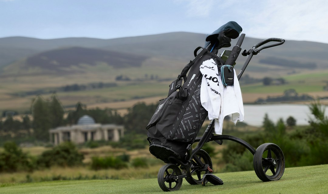 A golf bag strapped to a trolley on a green course with rolling hills