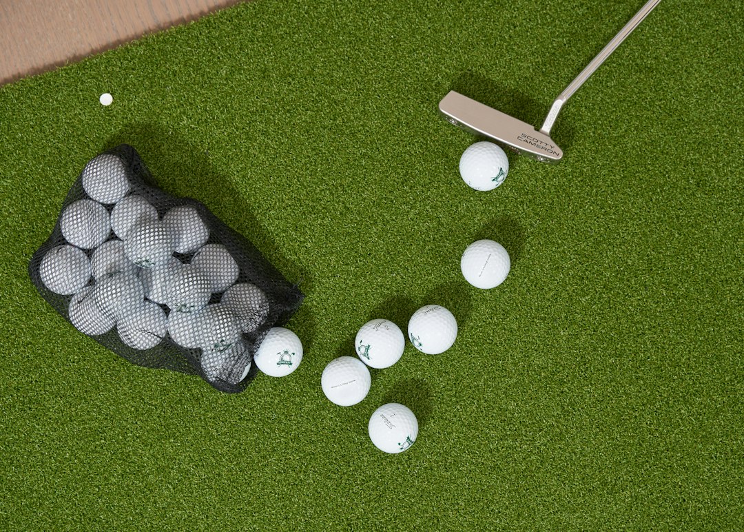 An indoor putting green with golf balls beside a mesh bag and a putter