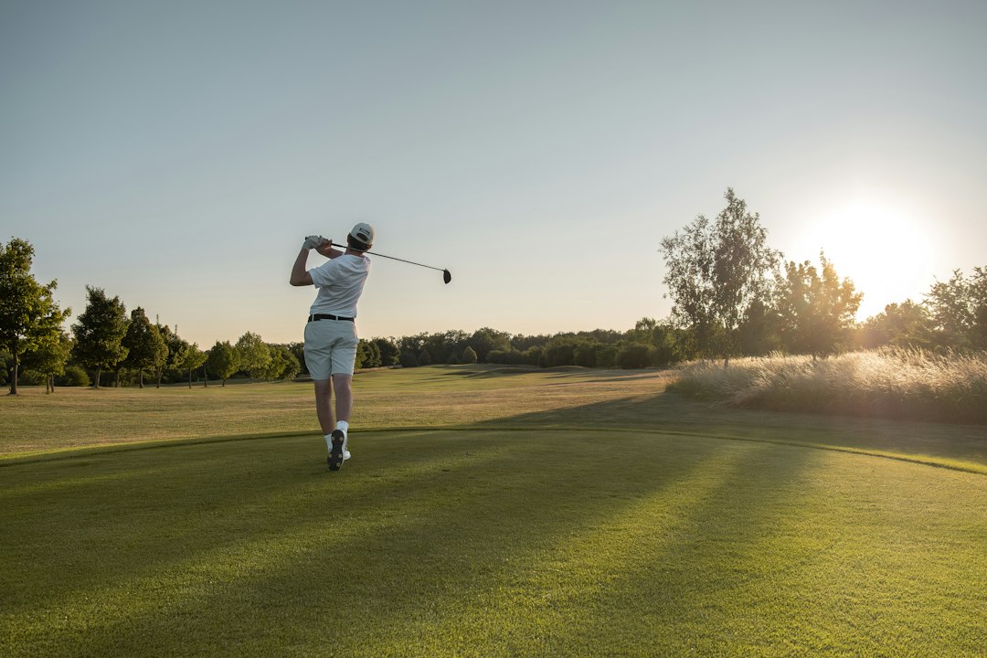 A golfer playing a shot on an open course in the sun